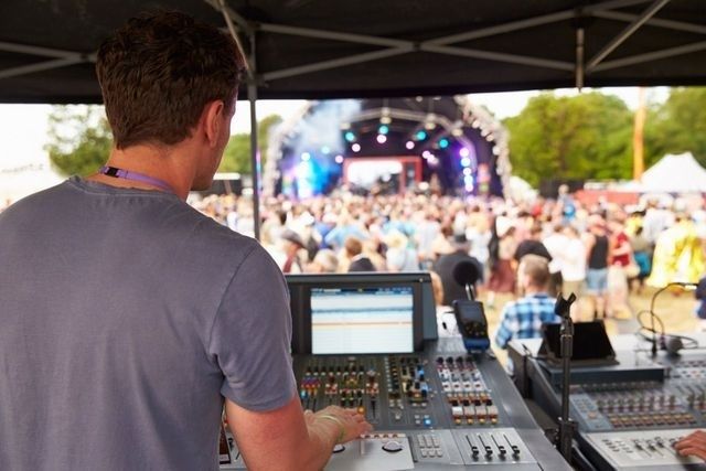 Sound engineer operates a mixing console overlooking a crowded festival stage
