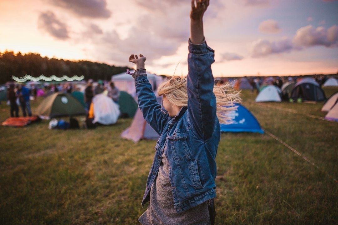 Festivalgoer raises both arms among tents at sunset