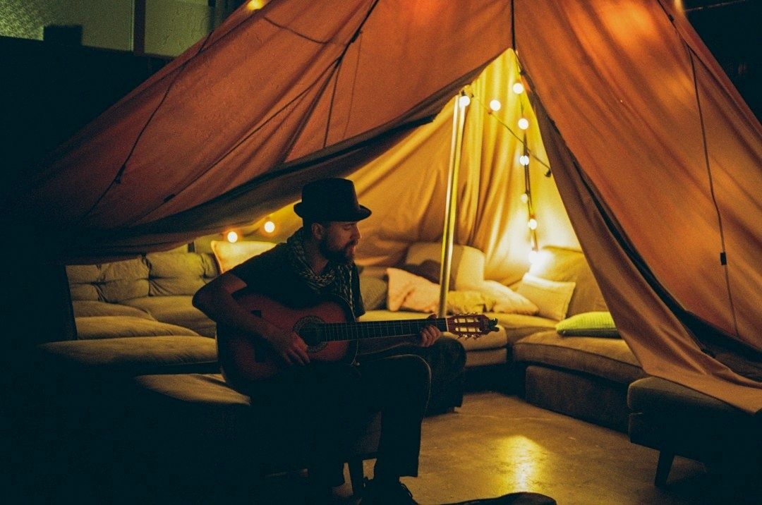 Person playing guitar inside a softly lit, tent-like lounge space