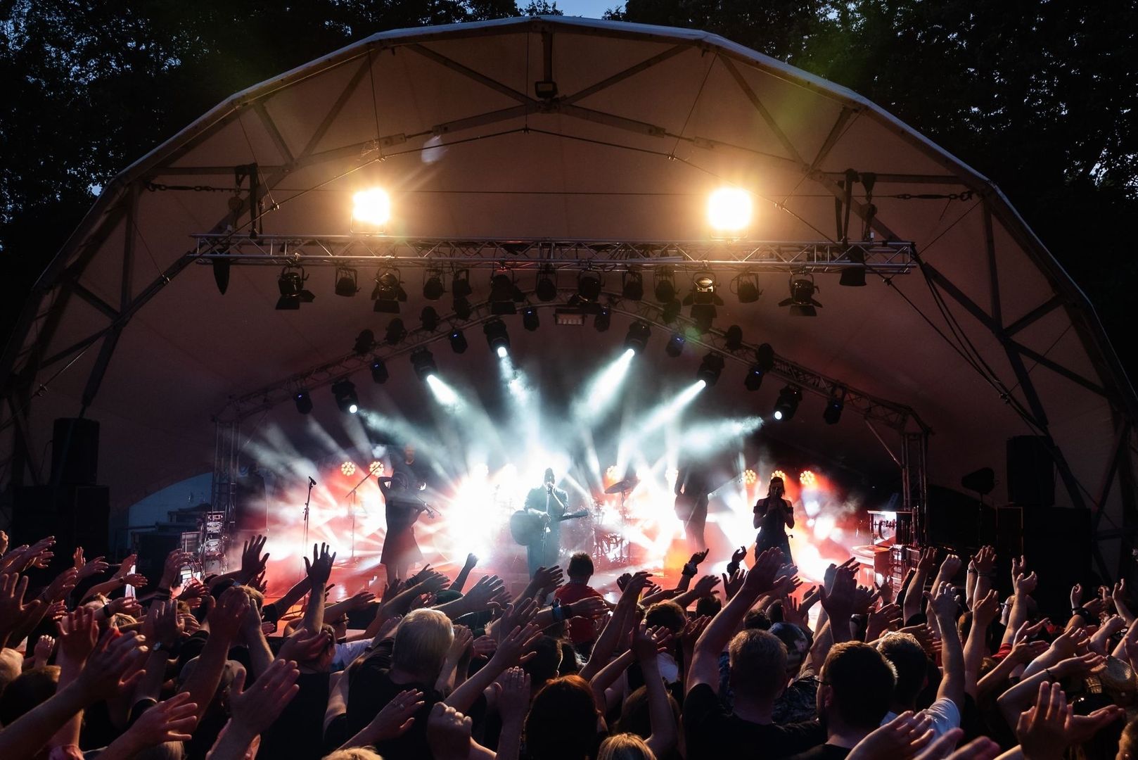 Crowd watching a brightly lit band perform under an outdoor festival canopy
